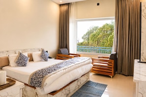 Una habitación de hotel con una cama grande, un escritorio, una silla y vista a árboles por la ventana.