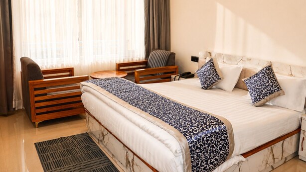 A hotel room with a bed, a wooden chair, a small table, a desk, and a telephone. - Shikhar Homestay (Lansdowne)