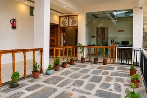 Un hall de hotel con piso de piedra, baranda de madera, plantas en macetas y una zona de recepción.