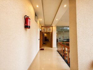 Un pasillo con extintor en la pared, barandilla de madera y macetas, y una puerta al final que da a otra habitación.