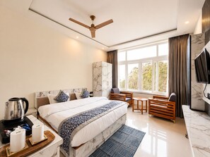 Una habitación de hotel moderna con una cama grande, un escritorio, una silla, un televisor y un ventanal con cortinas.