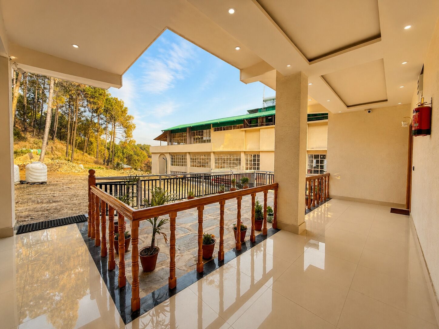 A spacious indoor area with a balcony overlooking a building with a green roof.