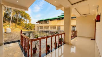 A spacious indoor area with a balcony overlooking a building with a green roof.