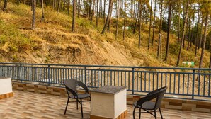 Een terras met twee rieten stoelen en een tafel, met uitzicht op een glooiend landschap met bomen.