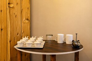 Una mesa de madera con tazas blancas, un tarro de cristal y un dosificador de azúcar de metal.