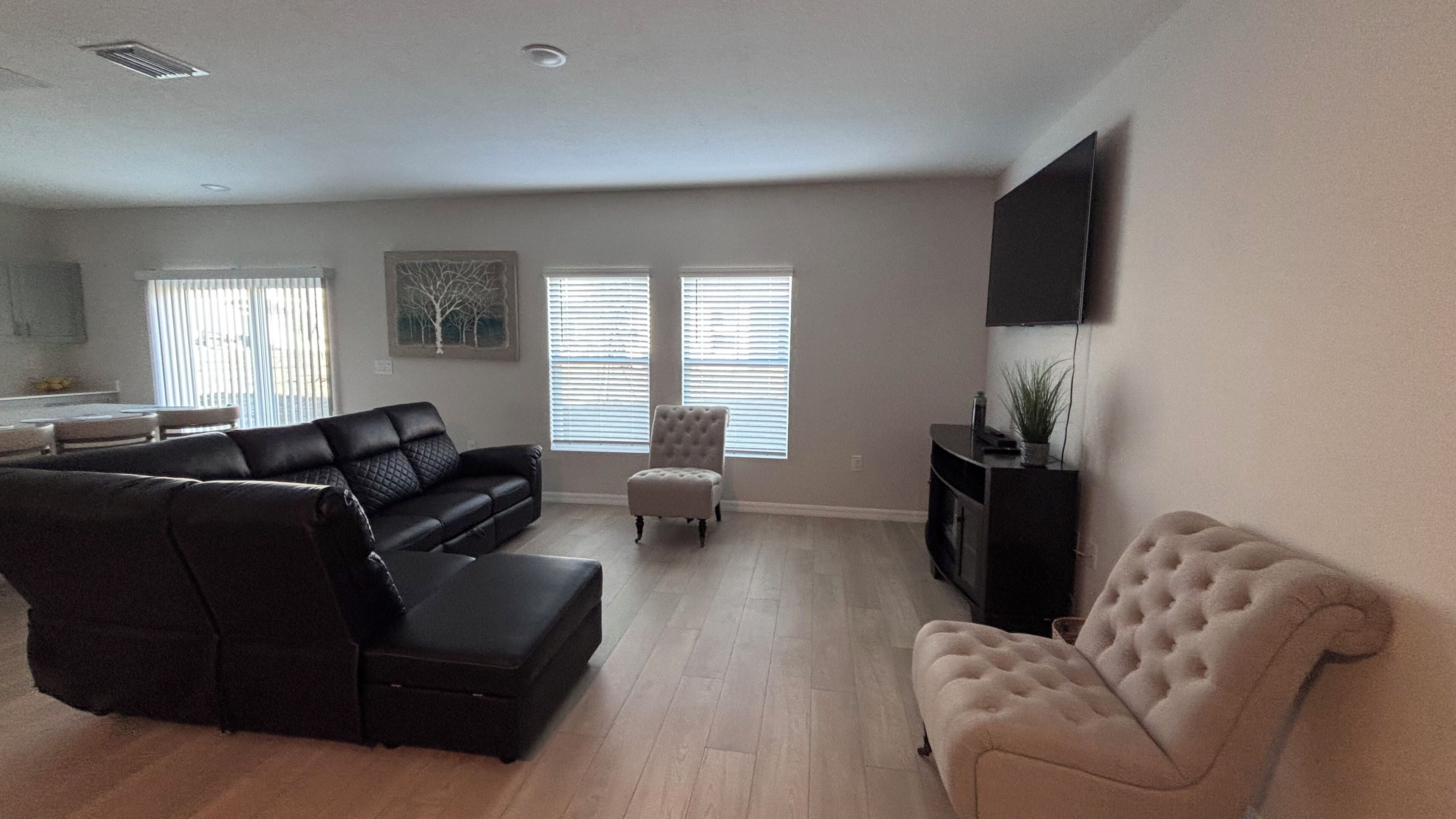 A living room with a sectional sofa, a loveseat, a small ottoman, and a television on the wall.