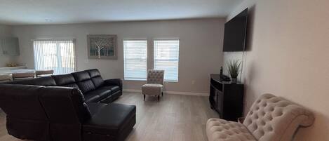 A living room with a sectional sofa, a loveseat, a small ottoman, and a television on the wall.