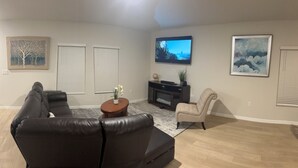 A living room with a black leather sofa, a beige armchair, a flat-screen TV mounted on the wall, and a painting above the TV. - Spacious 5 bedroom in Haines city, Florida for families sleeping up to 12 guests (Haines City)