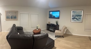 Ein Wohnzimmer mit schwarzem Ledersofa, einem beigen Sessel, einem Wand-Fernseher und einem Bild darüber.