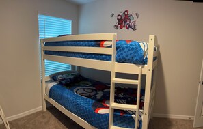 Un letto a castello con copriletto a tema Spider-Man, una finestra con persiane e un adesivo murale con i personaggi di Spider-Man.