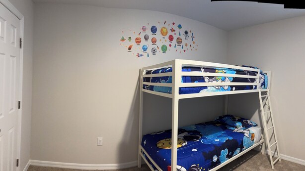 A bunk bed with a galaxy-themed mattress, a white wall with a space-themed decal, and a white door. - Spacious 5 bedroom in Haines city, Florida for families sleeping up to 12 guests (Haines City)