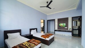 A hotel room with two beds, a ceiling fan, a TV, and a bathroom with a sink. - Hotel Amarendra stay in (Baramati)