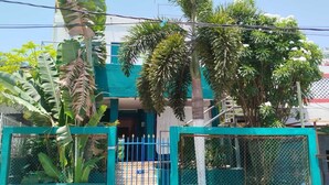 A residential building with a blue gate, surrounded by lush tropical vegetation.