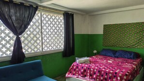 A room with a bed, a blue chair, and a window with a cross-patterned blind.