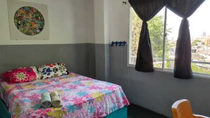 A bedroom with a bed, pillows, a window with curtains, a chair, and a wall with a circular artwork.
