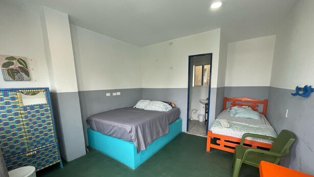 A small, compact room with two beds, a desk, and a chair.