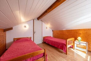 A room with two wooden beds, a white door, and a small bedside table with a lamp.