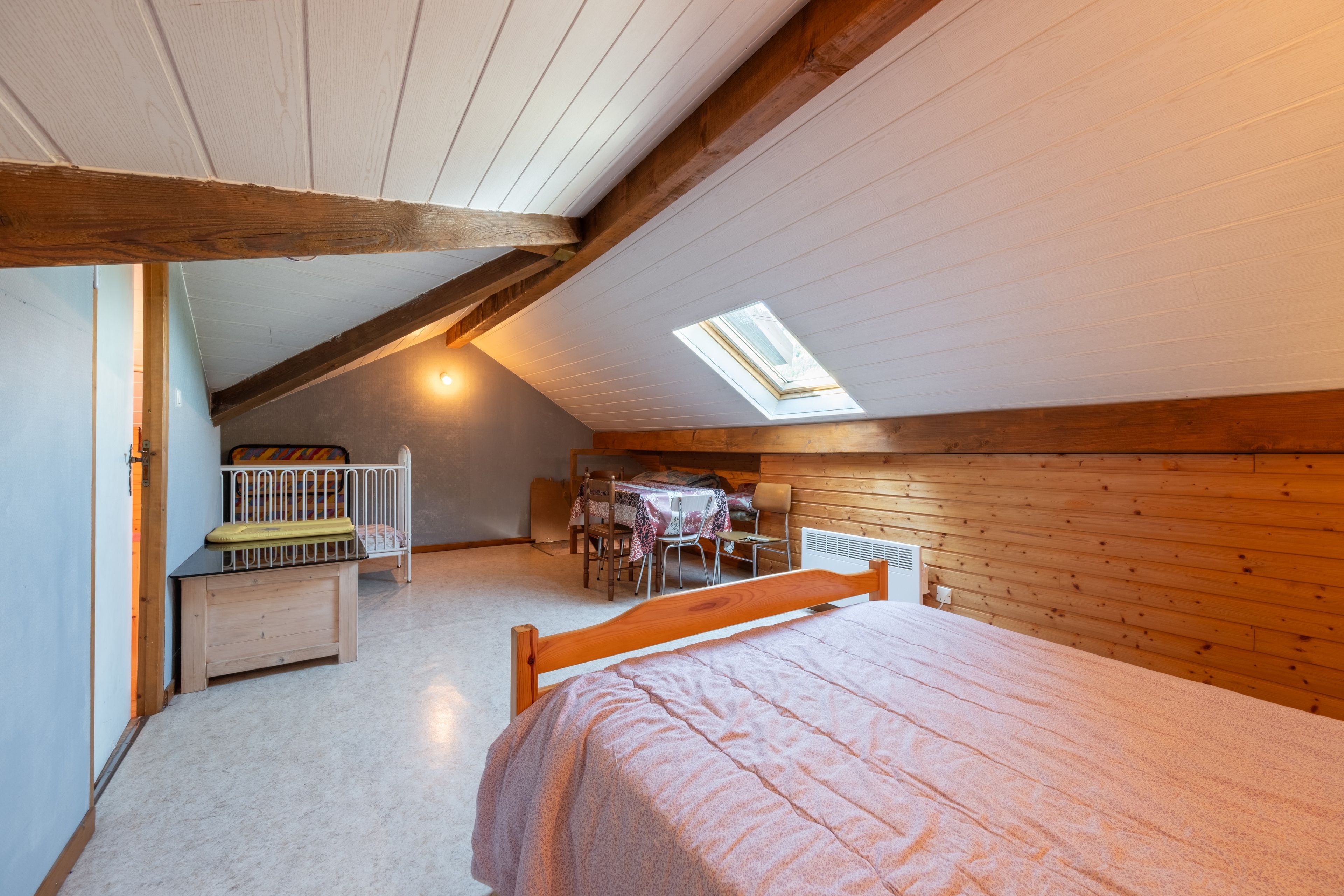 A bedroom with a sloped ceiling, a skylight, a bed, a small table with chairs, and a crib.