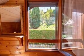 Interior de una cabaña de madera con vista por la ventana a un área con césped y árboles.