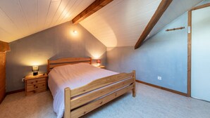 Un dormitorio con techo inclinado, una cama de madera, una mesita de noche y una lámpara fijada a la pared.