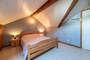 Un dormitorio con techo inclinado, una cama de madera, una mesita de noche y una lámpara de pared.