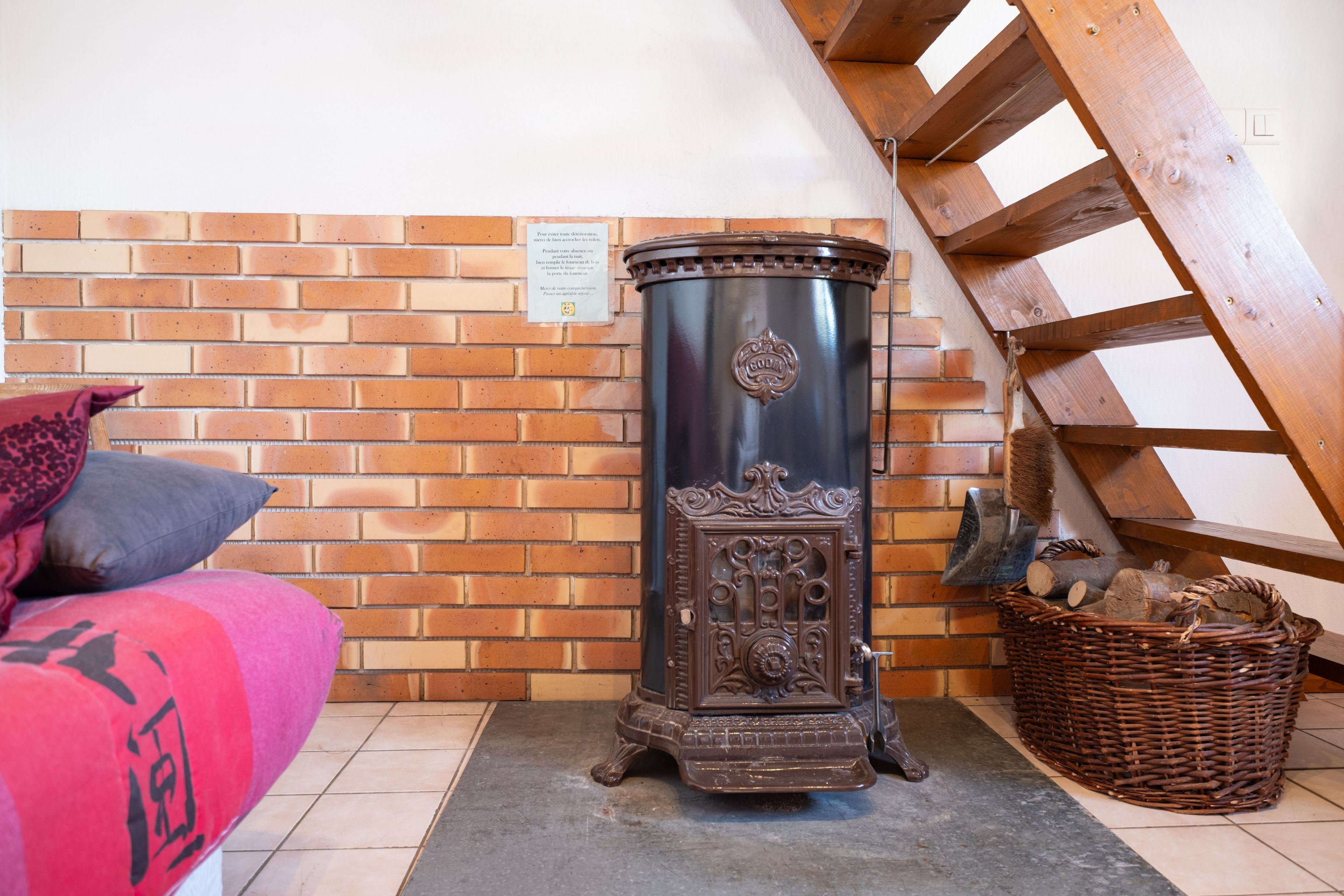 Une pièce avec un mur en briques, un escalier en bois, une cheminée et un lit avec des oreillers.