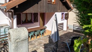 Un patio de piedra con mobiliario exterior, una mesa de madera y un área cubierta con un banco.