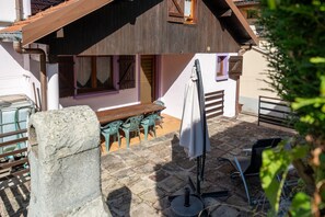 Un patio de piedra con mobiliario exterior, una mesa de madera y un área cubierta con un banco.