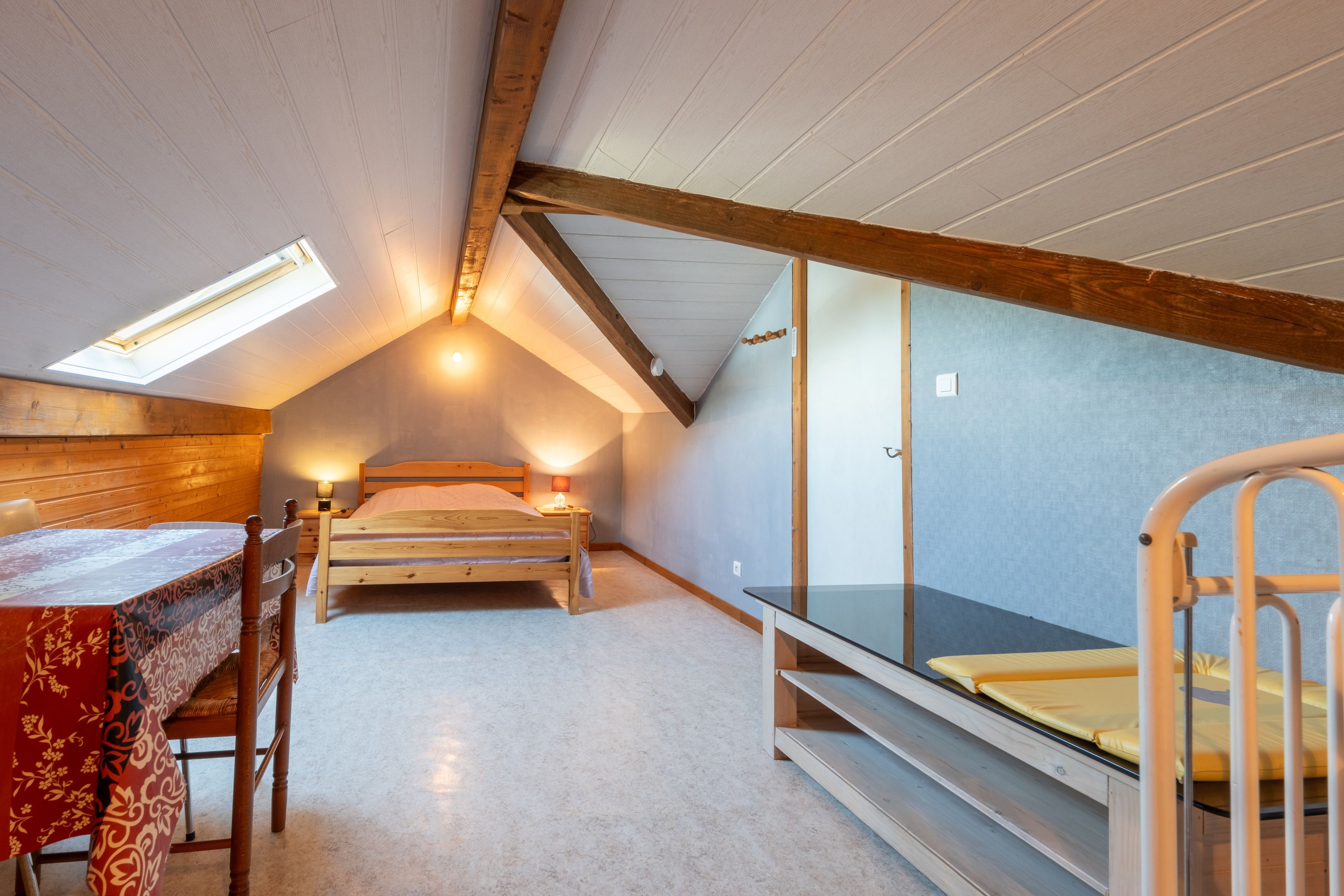 Una habitación con techo inclinado, una cama, una mesa con una silla y una litera.