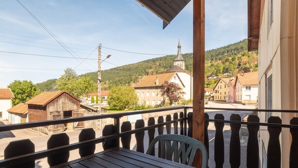 Un balcón de madera con vistas a un pueblo, incluyendo edificios y una colina.