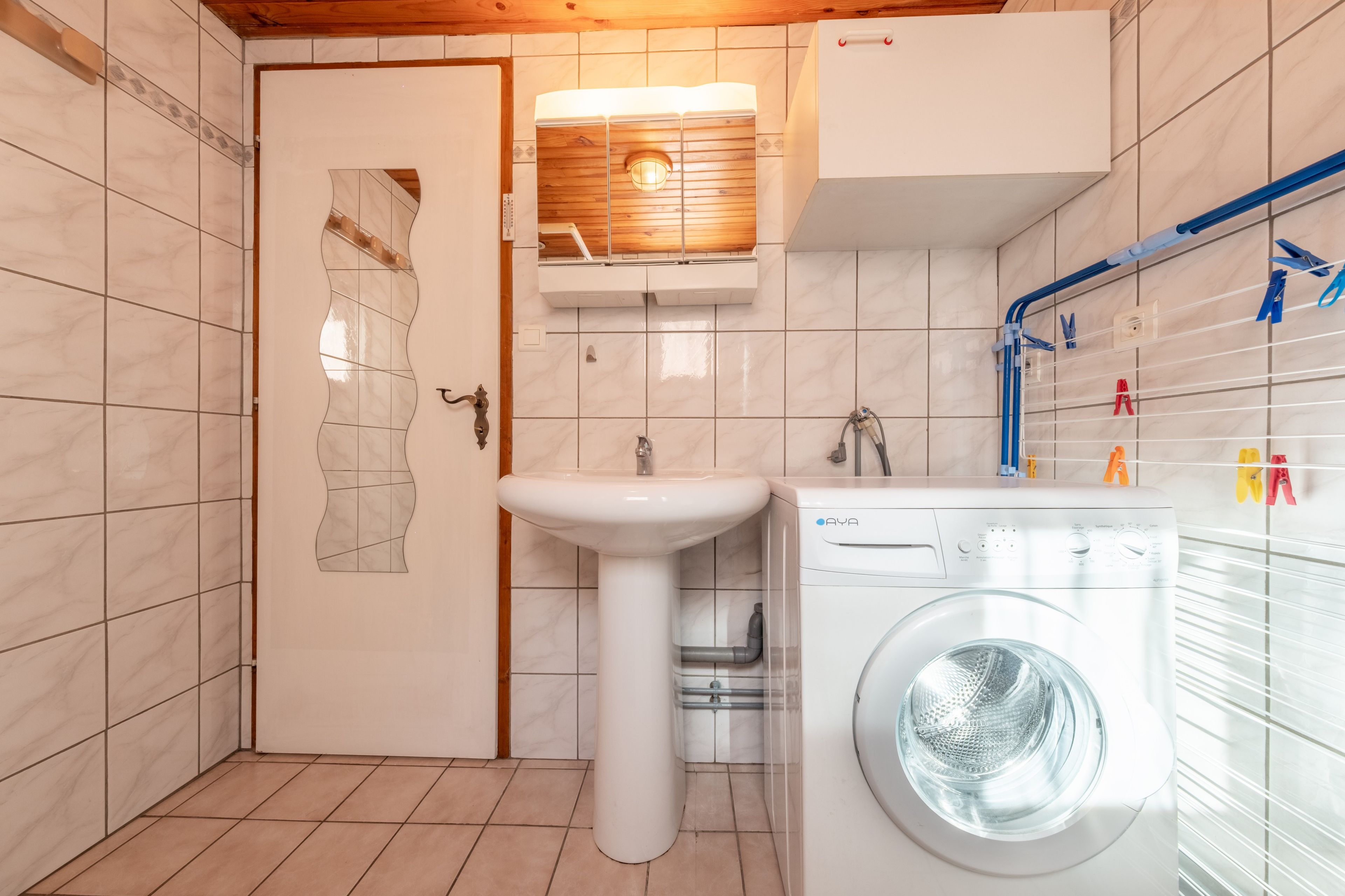 A compact bathroom with a sink, a washing machine, and a wooden cabinet.