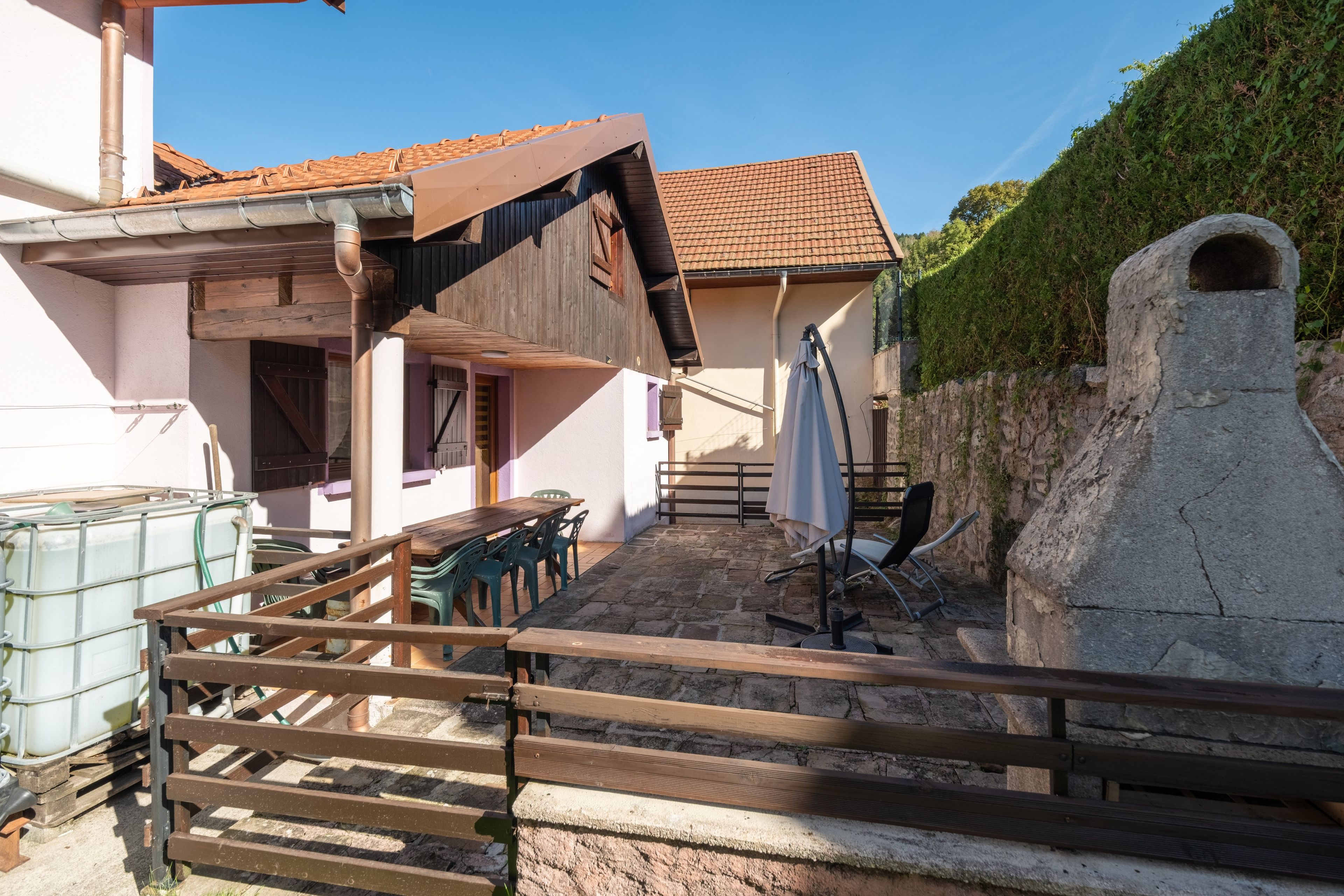 A courtyard with a wooden table and chairs, a stone wall, and a metal gate.