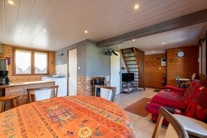 A cozy cabin interior with a dining area, a kitchen, a living room with a red sofa, and a TV.