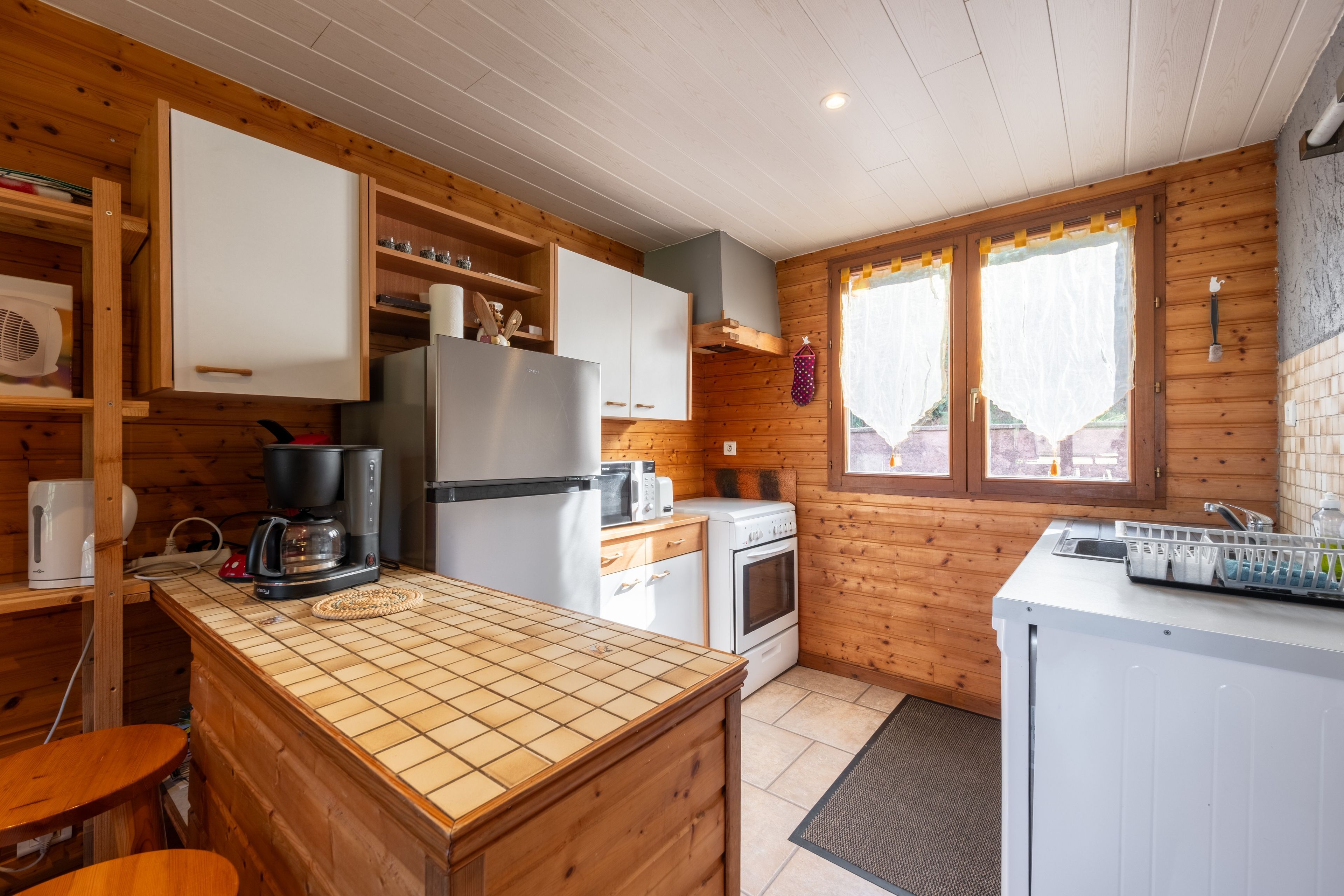 Eine kleine Küche mit Holzwänden, einem Kühlschrank, einer Kaffeemaschine, einer Mikrowelle und einem Spülbecken.