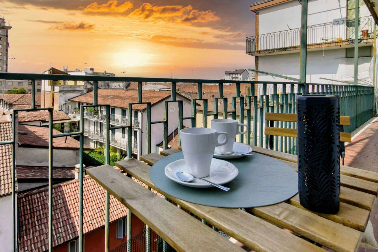 Ein Balkon mit einem Tisch für zwei Personen, mit Blick auf eine Stadtlandschaft bei Sonnenuntergang.