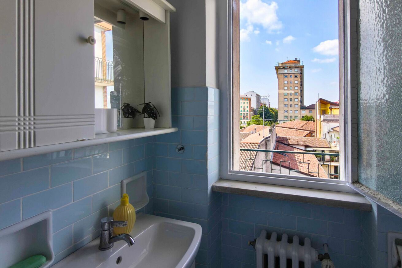 Ein Badezimmer mit Fenster, Waschbecken, Spiegel und Heizkörper.