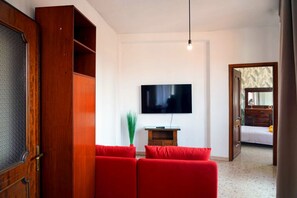 Ein Zimmer mit einem an der Wand befestigten Fernseher, einem Holzschrank und einem roten Sofa.