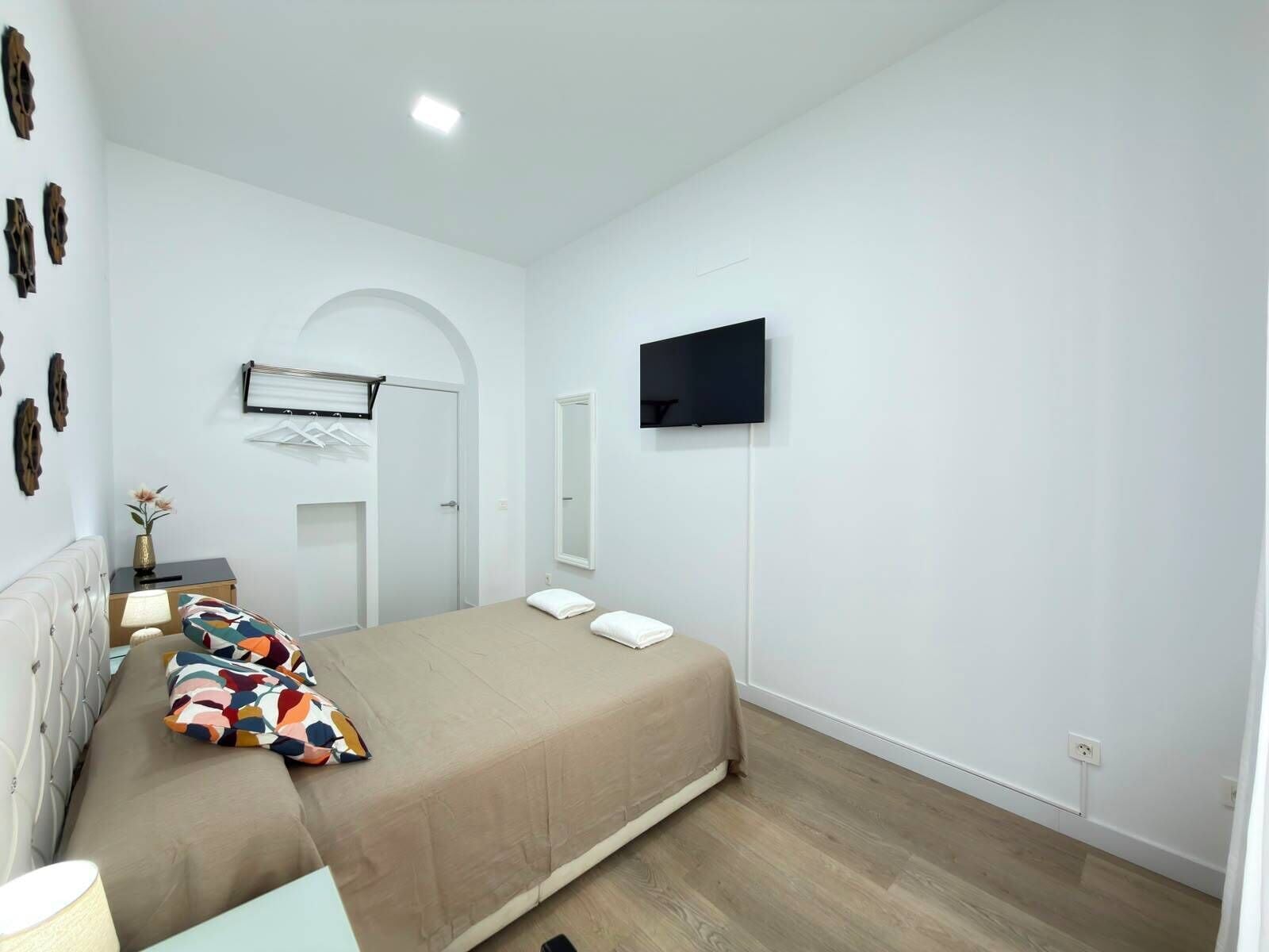 Un dormitorio moderno con una cama, un televisor montado en la pared y una mesita de noche con una lámpara.