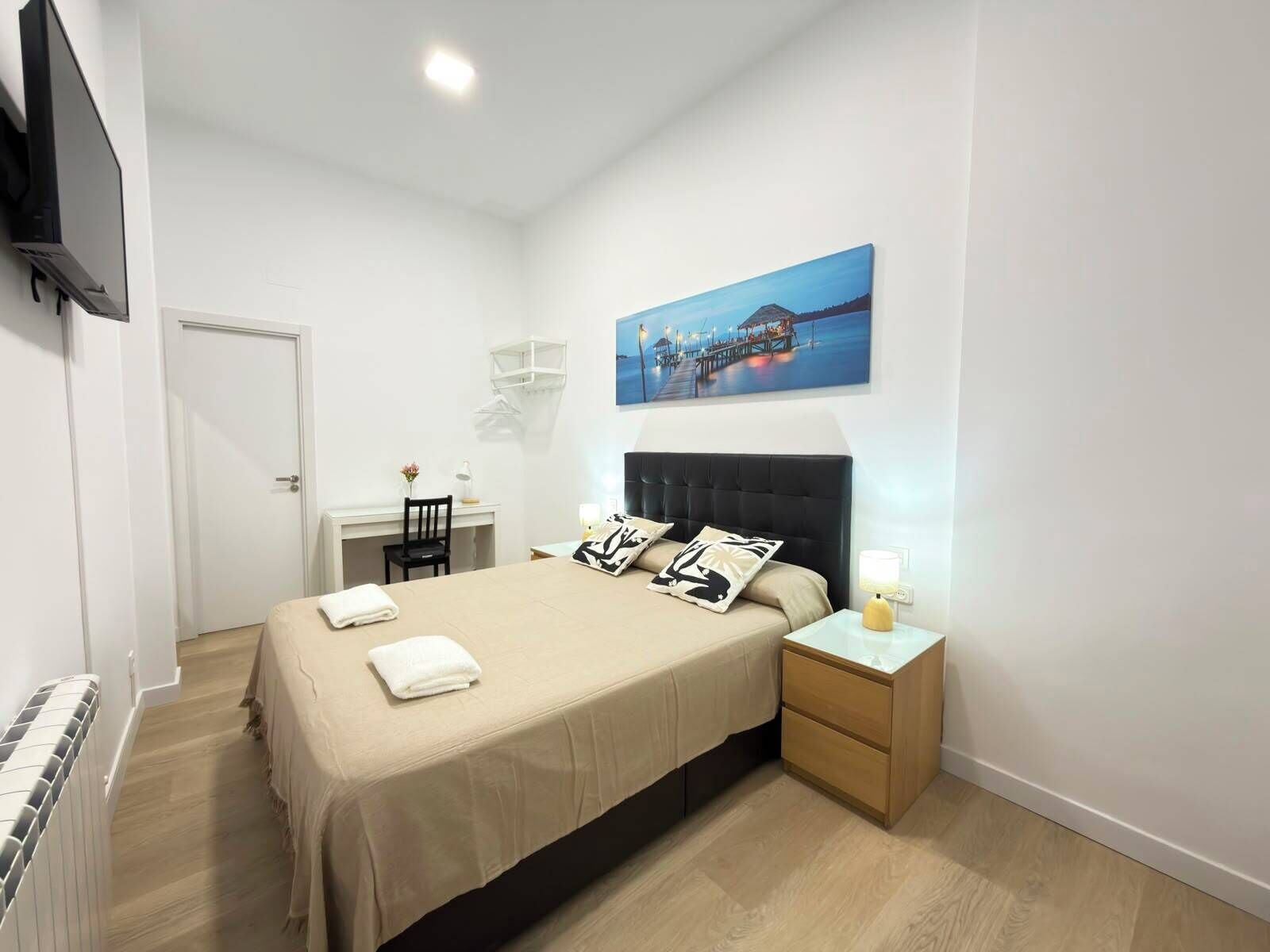 Una habitación de hotel con cama, mesita de noche, silla, escritorio y un cuadro en la pared.