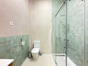 Un baño con inodoro, un cubo de basura y zona de ducha con mampara de vidrio.