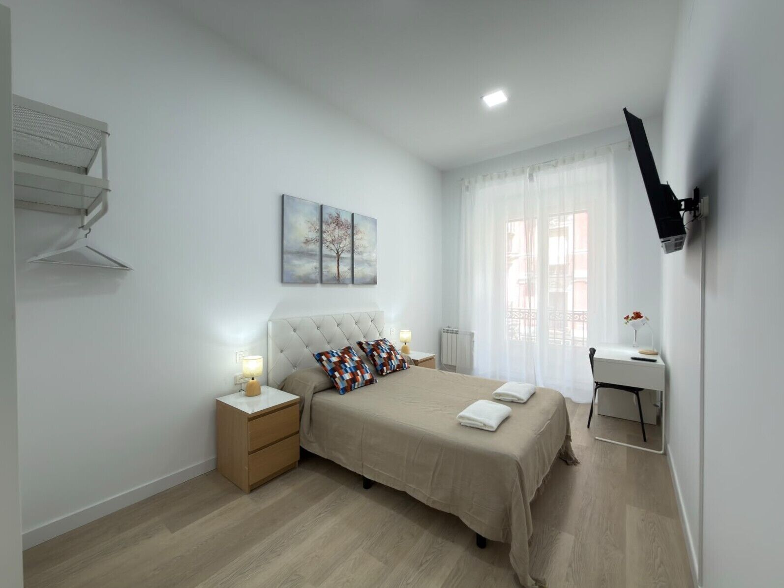 A bedroom with a bed, bedside tables, a desk, a chair, a TV, and a window with curtains.