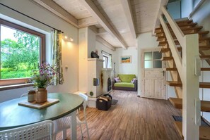 Un interior acogedor con una escalera de madera, un comedor con mesa y sillas, un sofá y vistas al exterior con vegetación.
