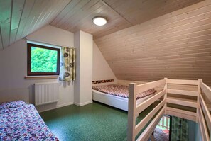 Una habitación con techo inclinado, una ventana con cortinas, una cama, un radiador y una litera.