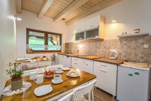 A kitchen with a wooden table, white chairs, a sink, and a window with a view.