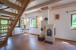 Una habitación con escalera de madera, chimenea, mesa de comedor con sillas y ventanas amplias.