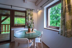 A room with a round table, white chairs, a potted plant, and a window with curtains.