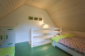 Una habitación con techo inclinado, una cama litera, un armario con pomos verdes y una alfombra verde.