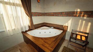 Un baño con una bañera de madera, una pared de ladrillo y una ventana con cortinas.