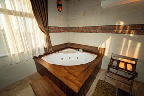 Un bagno con una vasca da bagno in legno, una parete in mattoni e una finestra con tende.