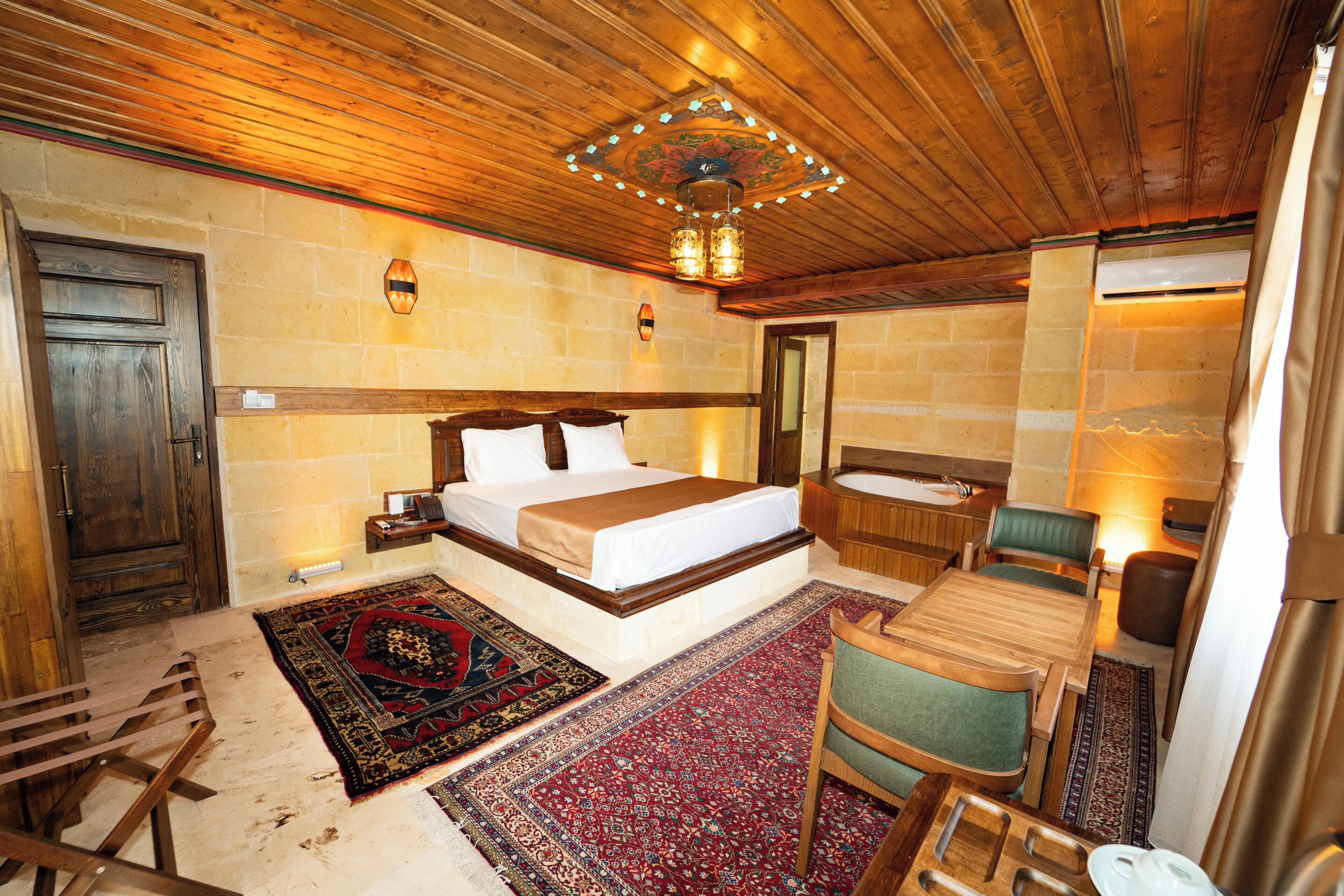 A hotel room with a large bed, a sitting area with a chair and table, a bathtub, and a wooden ceiling.